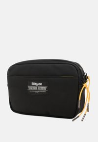 Pochette nera in nylon di forma rettangolare, con una zip gialla e una toppa con logo. Texture liscia con accenti a contrasto.