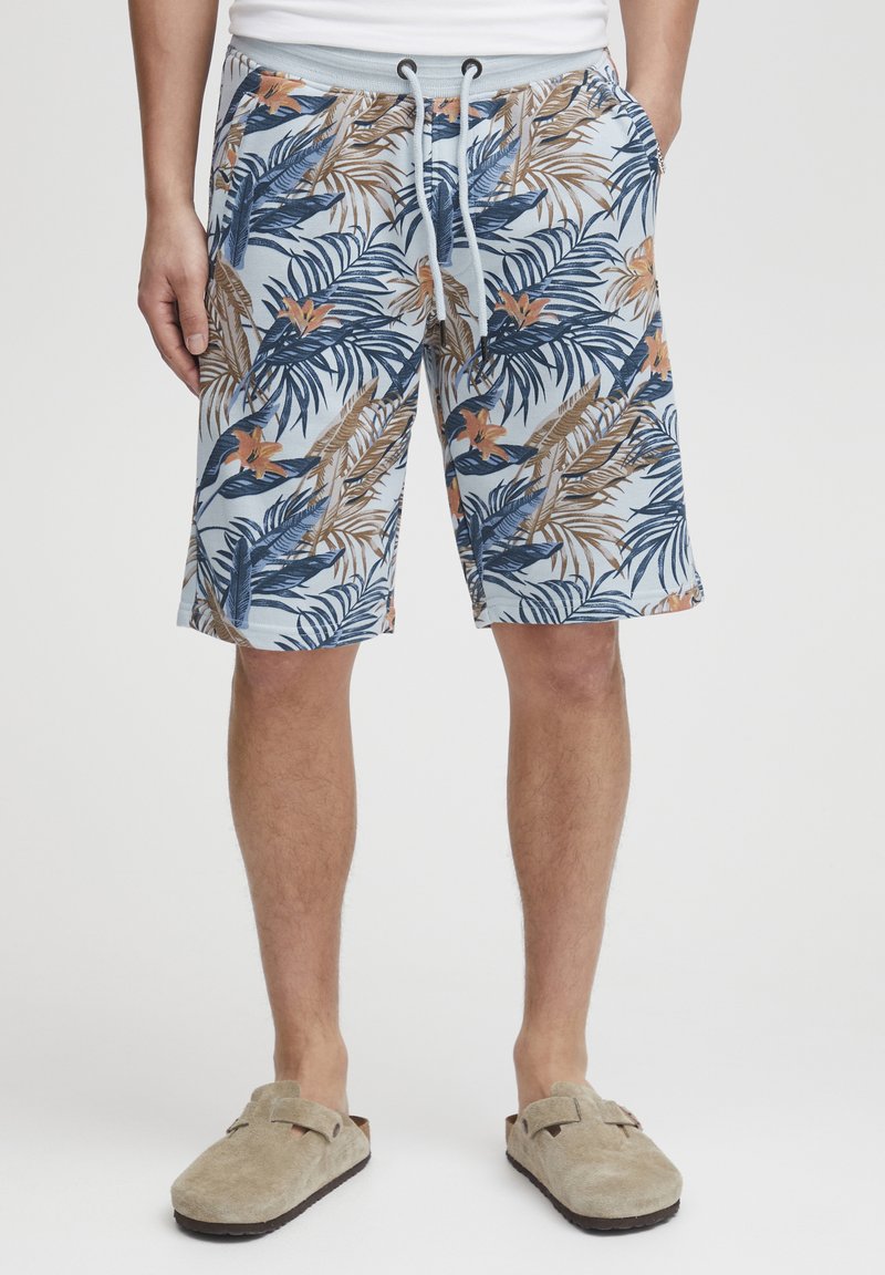 Un short bleu à motif arbore des feuilles de palmier et des motifs floraux en marine, brun et orange. Taille élastique avec un lien de serrage.