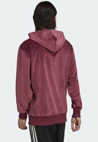 Tummanpunainen hupullinen collegepaita, jossa pehmeä, samettinen pinta. Siinä on rento istuvuus, resorit hihansuissa ja yksinkertainen, koristelematon muotoilu.