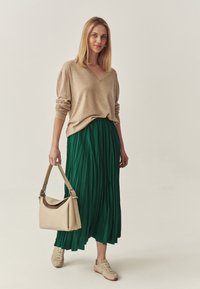 Beige v-hals trui, groene geplooide rok, tan handtas en tan sneakers. Eenvoudig ontwerp met een relaxte pasvorm en vloeiende materialen.