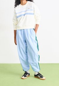 Ljusbeige sweatshirt med blå ränder, kombinerad med ljusblå baggybyxor med gröna sidostripes. Svarta sneakers med vita detaljer.