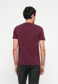 Burgunderfarget bomulls-T-skjorte med korte ermer, rund hals og glatt tekstur. Har et tettsittende design, synlige sømmer og detalj ved nakken bak.