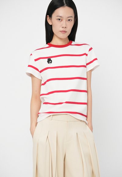 Camiseta branca com riscas horizontais vermelhas, decote redondo e mangas curtas. Apresenta um desenho bordado em preto na área do lado esquerdo do peito.