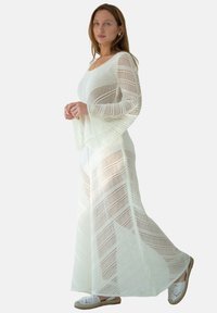 Długa, biała dziana sukienka w wzór chevron, z długimi rękawami i luźnym krojem. Połączona z białymi, plecionymi butami na wsuwkę.