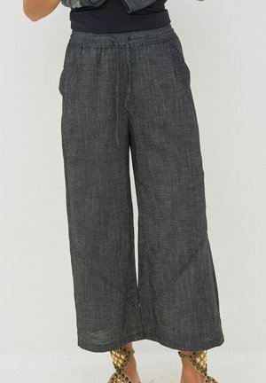 Wijde donkergrijze linnen broek met elastische tailleband en zakken, gedragen met gouden open teen hoge hakken.