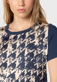 Top de manga corta con un patrón abstracto en azul marino y crema, con un collar sólido en azul marino y acentos de tela texturizada.