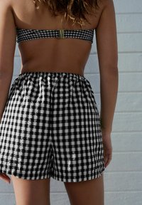 Schwarz-weiße Karo-Shorts mit einem elastischen Bund und einem taillierten, trägerlosen Oberteil mit einem Verschlussdetail auf der Rückseite.