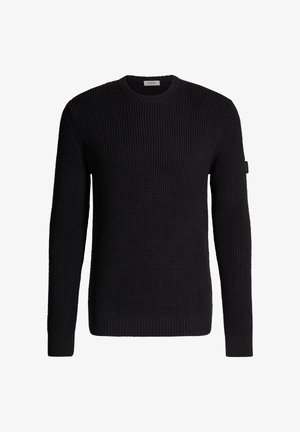 Pull noir à manches longues en maille avec col rond et poignets côtelés, présentant un motif gaufré texturé et un petit écusson sur la manche gauche.