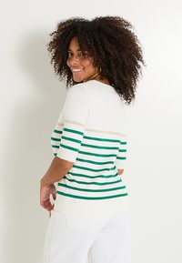Suéter de manga corta a rayas en color crema y verde con una franja dorada, cuello redondo y textura suave. Modelo mostrado de espaldas.