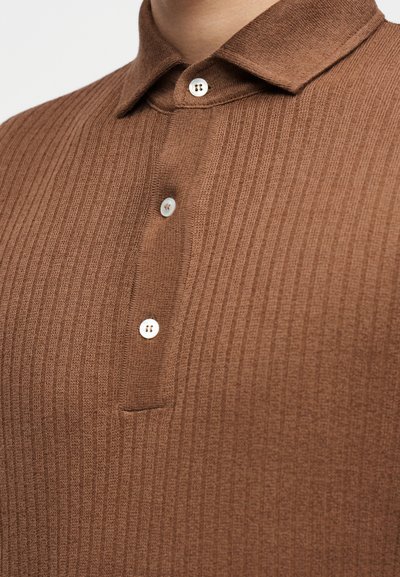 Polo marron côtelé en tissu texturé, avec un col à boutons et deux boutons blancs sur la patte de boutonnage.