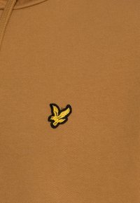 Felpa marrone con texture a coste caratterizzata da un piccolo logo di uccello ricamato in nero e giallo sul petto.