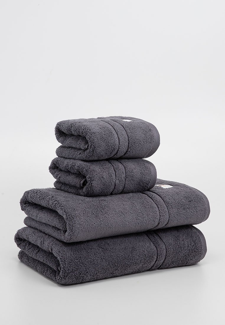Stapel aus vier dunkelgrauen Handtüchern, zwei große gefaltet und flach sowie zwei kleinere aufgerollt oben drauf, auf einem schlichten hellen Hintergrund präsentiert.