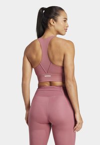 Sujetador deportivo rosa y leggings de tiro alto hechos de una tela elástica; cuenta con un diseño de espalda nadadora y detalles de costura sutiles.