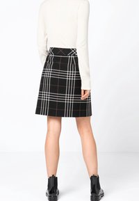 Jupe à carreaux noirs avec des rayures blanches et brunes, présentant une coupe ajustée et un tissu texturé. Assortie à des bottines noires, vue de derrière.