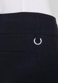 Černé kalhoty vyrobené z hladké tkaniny, které mají boční kapsu a stříbrný kruhový kovový detail na pasu.