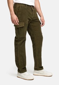 Olivengrønne corduroy cargo bukser med lige pasform, som har sidelommer, struktureret stof og knaplukning. Kombinert med hvite sneakers.