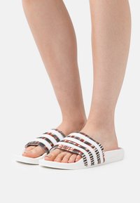 Σαμπό με λευκή σόλα, που διαθέτει πολύχρωμο πλεχτό πάνω μέρος με μαύρες, κόκκινες και λευκές ρίγες. Σχεδίαση ανοιχτού δαχτύλου.