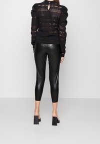 Černá strukturovaná blůza s nafouknutými rukávy a designem klíčové dírky na zadní straně. V kombinaci s upnutými, lesklými černými koženými legínami a muly na blokovém podpatku.