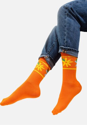 Pomarańczowe skarpety z żółtym wzorem kwiatowym, z zielonymi i niebieskimi akcentami. Wykonane z cienkiego, teksturowanego materiału z prążkowanym mankietem.