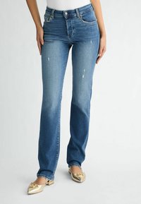 Heled sinise fade'iga sirged denim teksad, millel on kulunud kohad. Ühendatud sädelevate kuldsete lakk kingadega, millel on terav nina.