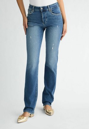 Jeans in denim dalla sfumatura chiara a quella scura, con taglio dritto e zone sfilacciate. Abbinati a ballerine dorate lucide con punta affusolata.