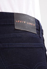 Jeans de mezclilla azul oscuro con una etiqueta de cuero en la cintura que tiene "LEVI'S LINE 8" grabado en rojo, costuras contrastantes y un diseño de corte ajustado.