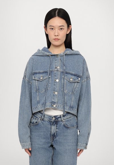 Kuttet lys blå denimjakke med hette, knappelukking, to brystlommer og snor. Sammen med matchende denim-bunn.