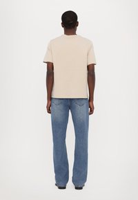Beige bomulds t-shirt med rund halsudskæring, parret med blå jeans med lige ben, der har diskrete syninger og en struktureret overflade.