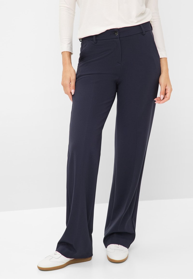 Pantalons larges bleu marine en tissu lisse. Présente une fermeture à bouton et des poches inclinées sur les côtés. Taille ajustée.