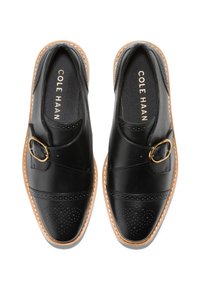 Černé kožené mokasíny s perforovaným vzorem, zlatou sponou a hnědým gumovým podpatkem. Vyznačují se pohodlným nazouvacím stylem a elastickými bočními panely.