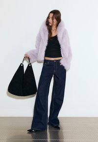 Lilac faux furjakke, tætsiddende sort tanktop, brede mørke denimjeans og en sort ruskinds taske med metaldetaljer, mod en ensfarvet baggrund.