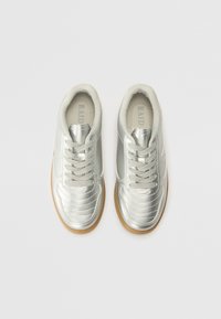 Silberne Sportschuhe mit einem glatten, glänzenden Obermaterial aus synthetischem Material, Gummisohlen und sechs Ösen für die Schnürsenkel. Gepolsterte Zunge und Kragen.