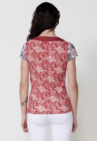 Rotem T-Shirt mit floralem Muster und kurzen Ärmeln; weiße Akzente an den Ärmeln und am Kragen. Glatte Textur, figurschmeichelnde Form und runder Halsausschnitt.