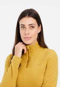 Pullover in pile giallo senape, con collo a zip a un quarto, maniche lunghe e dettaglio con logo. Tessuto morbido, design caldo.