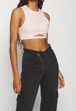 Light pink sleeveless crop top with a cutout detail and ribbed texture, paired with high-waisted black cargo pants featuring a zip closure.