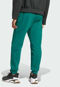 Πράσινα αθλητικά κολάν με λείο υφασμά, ελαστική μέση και σφιχτές μανσέτες. Συνδυασμένα με μαύρα και άσπρα αθλητικά παπούτσια.