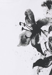 O tecido branco apresenta um grande padrão floral preto com salpicões subtis. O design inclui pétalas detalhadas e elementos florais distintos.