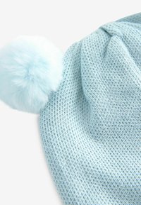 Ljusblå stickad mössa med en fluffig pom-pom på toppen. Texturen är mjuk och har ett fint vävmönster samt en något nedhasad design.