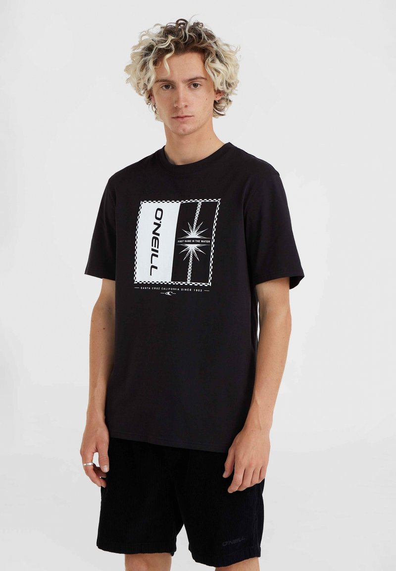 Camiseta negra con un estampado gráfico blanco, que presenta un borde a cuadros y texto, combinada con pantalones cortos de pana negra texturizada.