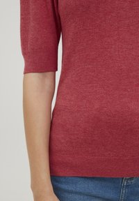 Röd stickad tröja med korta ärmar, rundad halsringning och en mjuk textur. Har en ribbad fåll och en slät tygfinish.