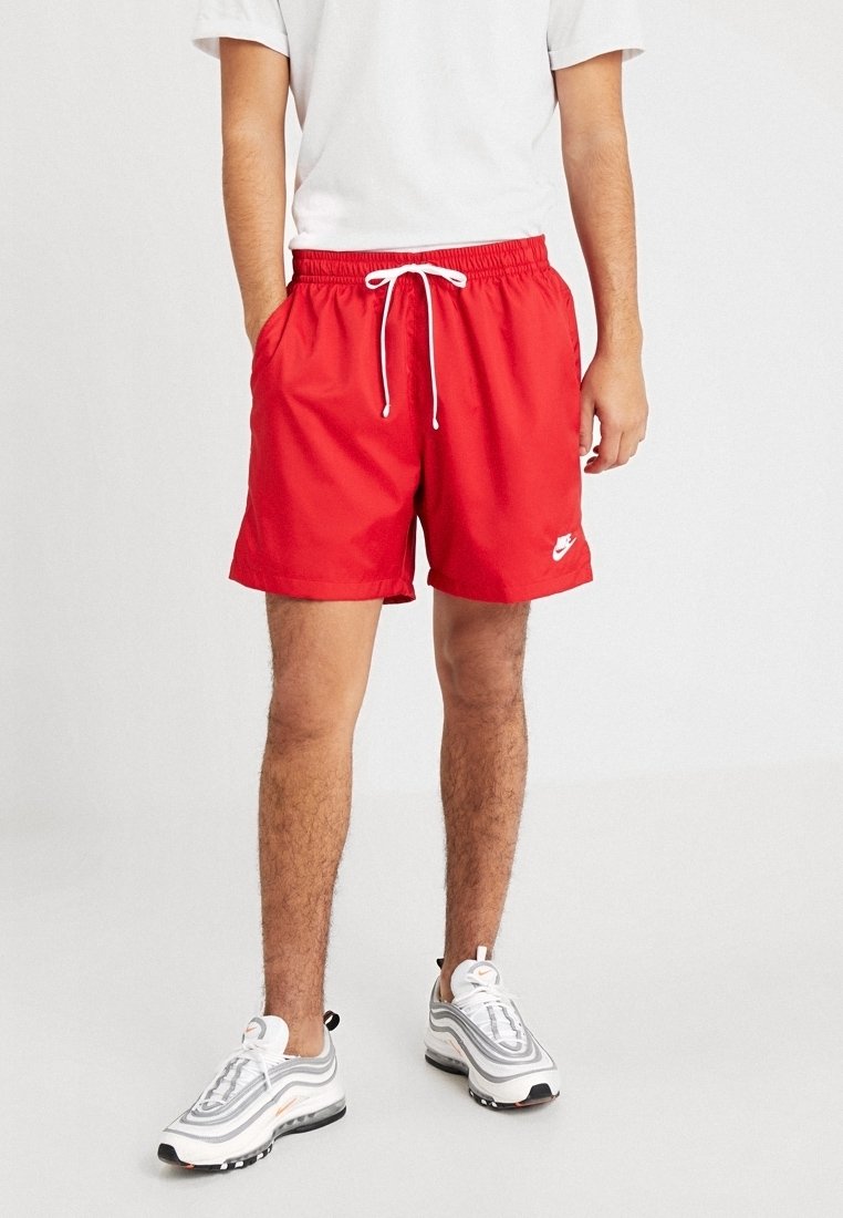 Červené sportovní šortky vyrobené z lehké tkaniny, s elastickým pasem na šňůrku, bočními kapsami a bílým logem Nike na lemu.
