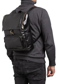 Zaino in pelle nera con chiusura a pattina, tasca frontale con zip e spallacci regolabili. Texture liscia, accessori minimi e design moderno.