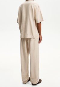 Camicia beige a maniche corte e pantaloni larghi abbinati in un tessuto testurizzato, con colletto e tasca laterale sui pantaloni.