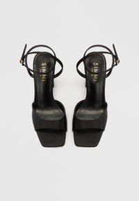 Μαύρα ψηλοτάκουνα σανδάλια με κομψό σχέδιο, που διαθέτουν τετράγωνη μύτη και λεπτά λουριά στον αστράγαλο. Κατασκευασμένα από απαλό υλικό με ματ φινίρισμα.