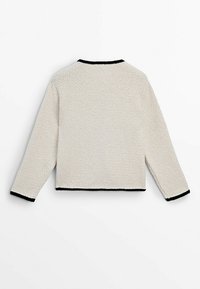 Kremowy, krótki sweter z teksturowanym splotem, z czarnym wykończeniem wzdłuż dekoltu i mankietów.