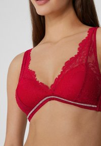 Bralette de encaje rojo con escote en V profundo, tirantes anchos de encaje y un detalle decorativo de rhinestones a lo largo de la banda. Tejido suave y texturizado.