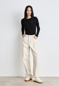Black long-sleeve shirt with blue logo, paired with cream wide-leg pants and white sneakers featuring yellow accents and gum sole.