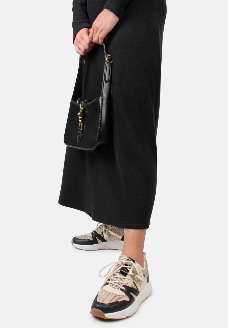 Robe noire mi-longue, associée à des baskets beiges et noires avec un design texturé ; sac à main noir brillant avec quincaillerie dorée.