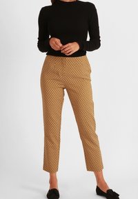 Pantalons marron à motifs avec une coupe fuselée, fabriqués en tissu léger, associés à un haut noir près du corps et des ballerines noires.