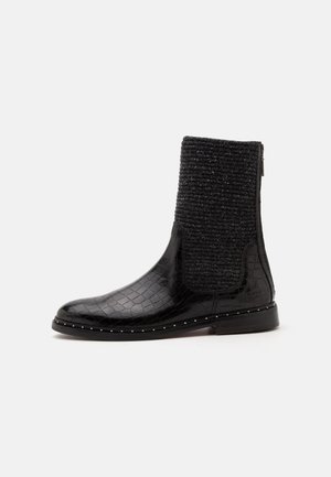 Botte noire mi-mollet avec texture crocodile brillante, dessus en tissu tricoté, fermeture éclair latérale et petits clous métalliques le long du bord de la semelle.